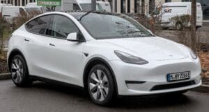 Vue de profil d'une Tesla Model Y blanche sur route, illustrant son design et ses dimensions