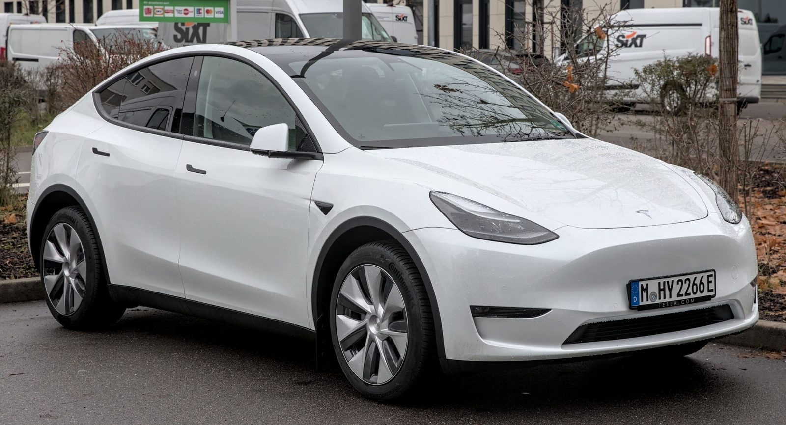 Vue de profil d'une Tesla Model Y blanche sur route, illustrant son design et ses dimensions