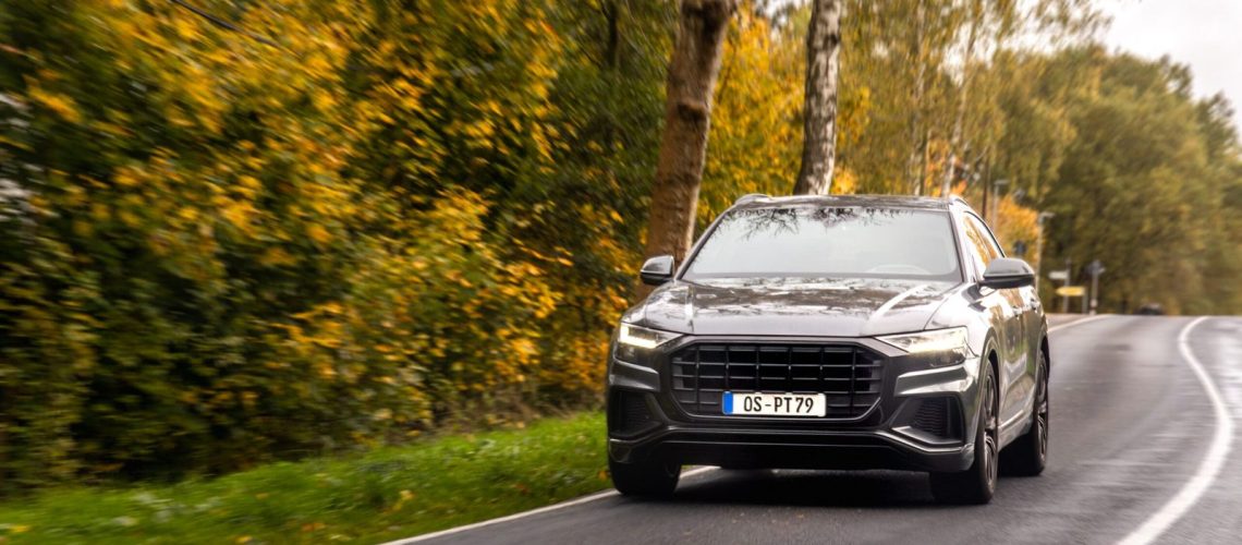 A stylish crossover drives on a damp road framed by golden fall trees, capturing autumn mood, power, and freedom.