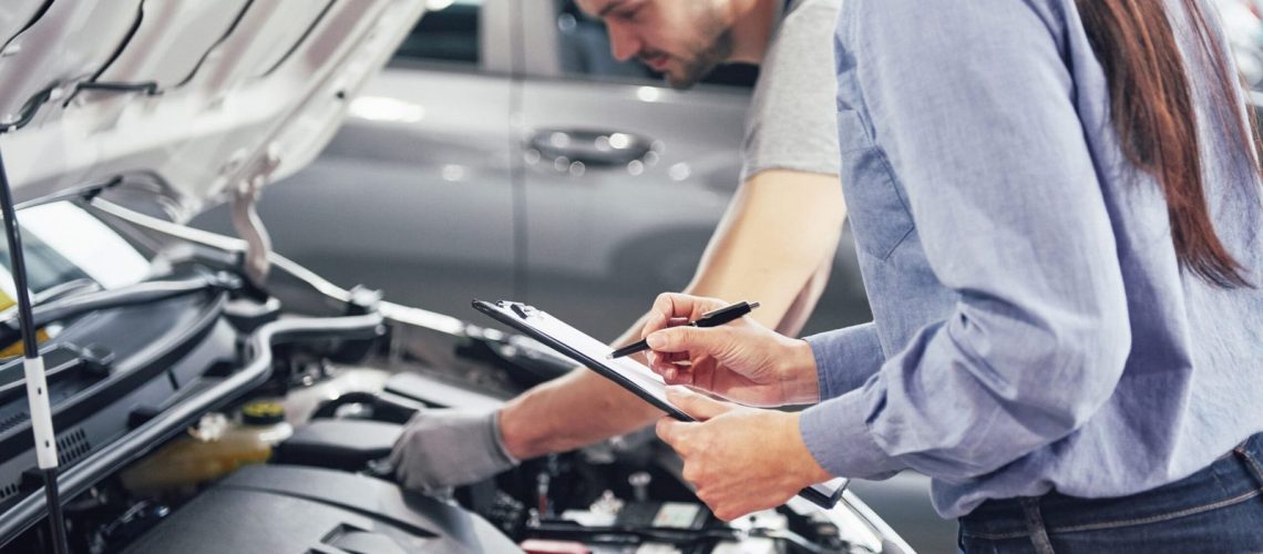 A man mechanic and woman customer look at the car hood and discuss repairs