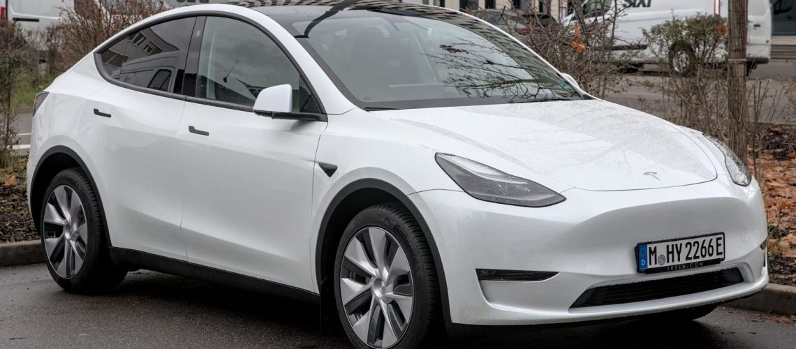 Vue de profil d'une Tesla Model Y blanche sur route, illustrant son design et ses dimensions